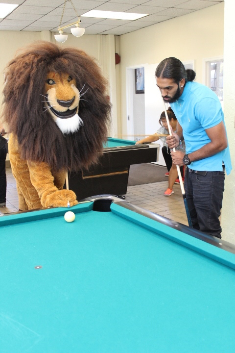 Student posed with Nassau Mascot Leo the Lion playing billiards in game room